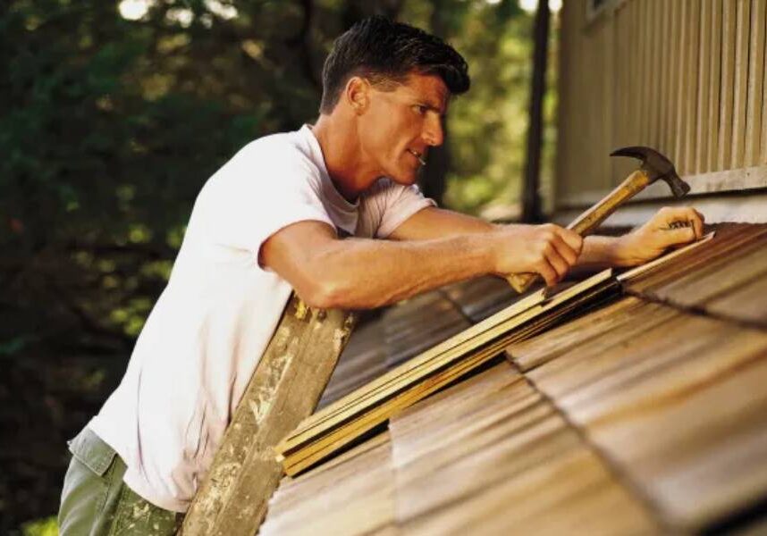 A man is hammering a shingle on a roof.
